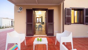 Une terrasse extérieure avec deux chaises blanches, une petite table avec des boissons et une serviette colorée.