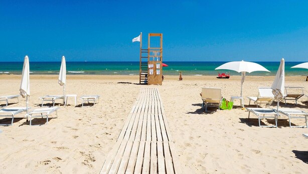 Une plage avec une promenade en bois menant à la mer, des chaises de plage blanches et des parasols.