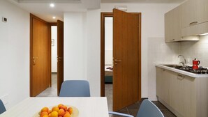 Une cuisine compacte avec un coin repas, comprenant une cuisinière, un évier et une table agrémentée d’un panier de fruits.