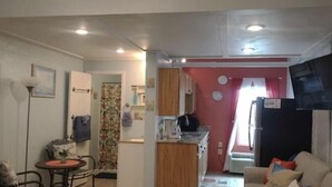 A compact living space with a kitchen, dining area, and a living room. A 'Welcome to Paradise' sign is visible above the kitchen.