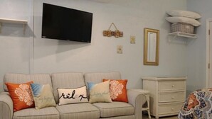 A living room with a sofa, a television, a dresser, and a bed.