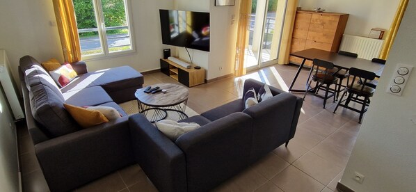 A living room with a sofa, a coffee table, a TV, and a dining area with chairs. - Bright and modern apartment (Prévessin-Moëns)
