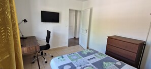 A bedroom with a bed, a desk, a chair, a TV, a dresser, and a door leading to another room. - Bright and modern apartment (Prévessin-Moëns)