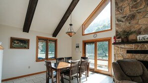 Un espace repas avec une table et des chaises en bois, de grandes fenêtres, un mur en pierre et une cheminée.