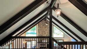 Une chambre mansardée avec un plafond en pente, des poutres apparentes, un mur en pierre et un escalier menant à un niveau supérieur.