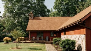 Une cabane rustique avec des fondations en pierre, un toit en briques et une terrasse en bois équipée de chaises.