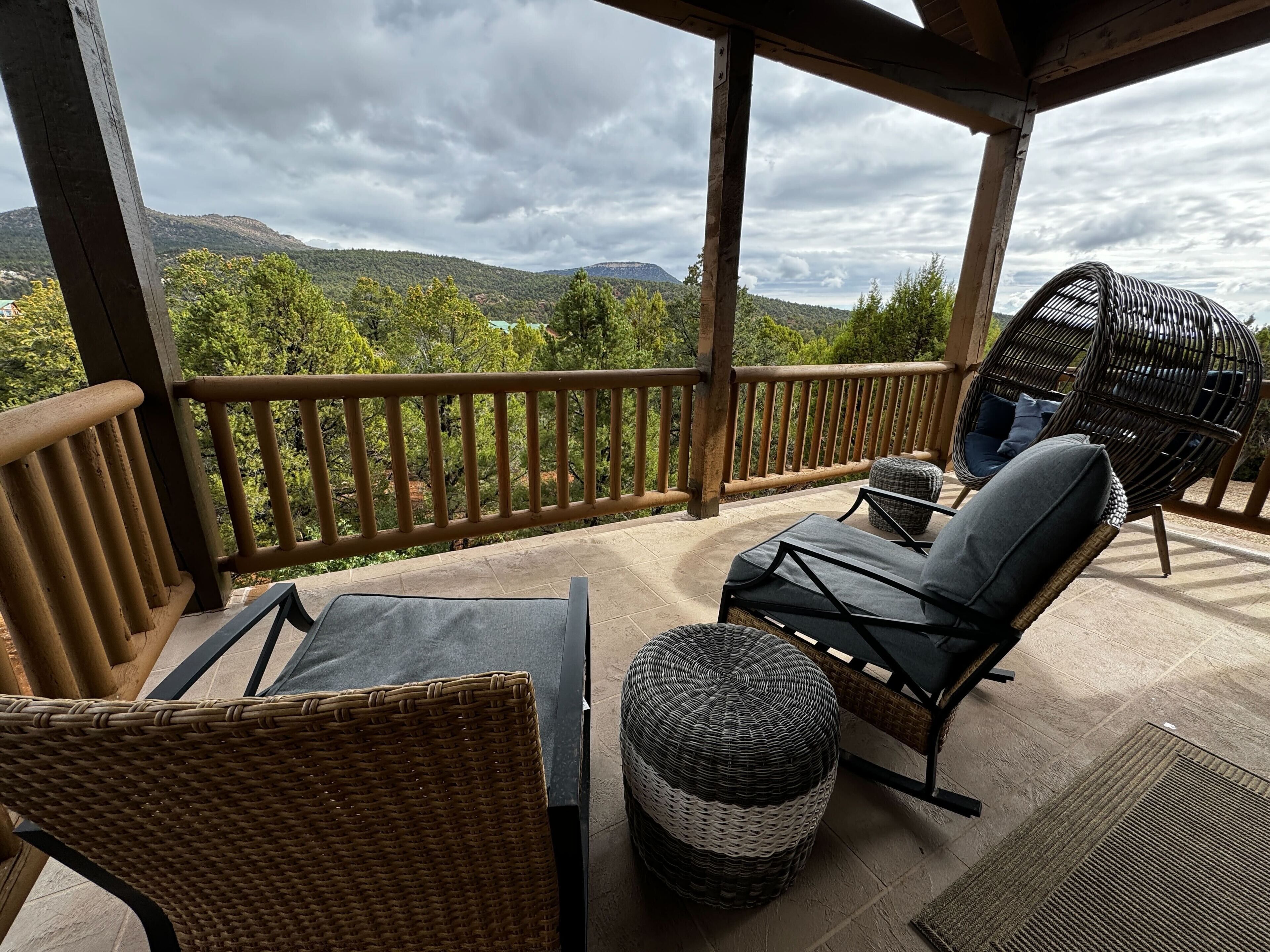 A covered outdoor seating area with wicker furniture, a cushioned chair, and a view of green hills.