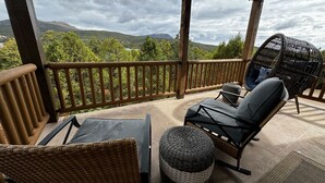 Een overdekt terras met rieten meubels, een comfortabele fauteuil en uitzicht op glooiende heuvels.