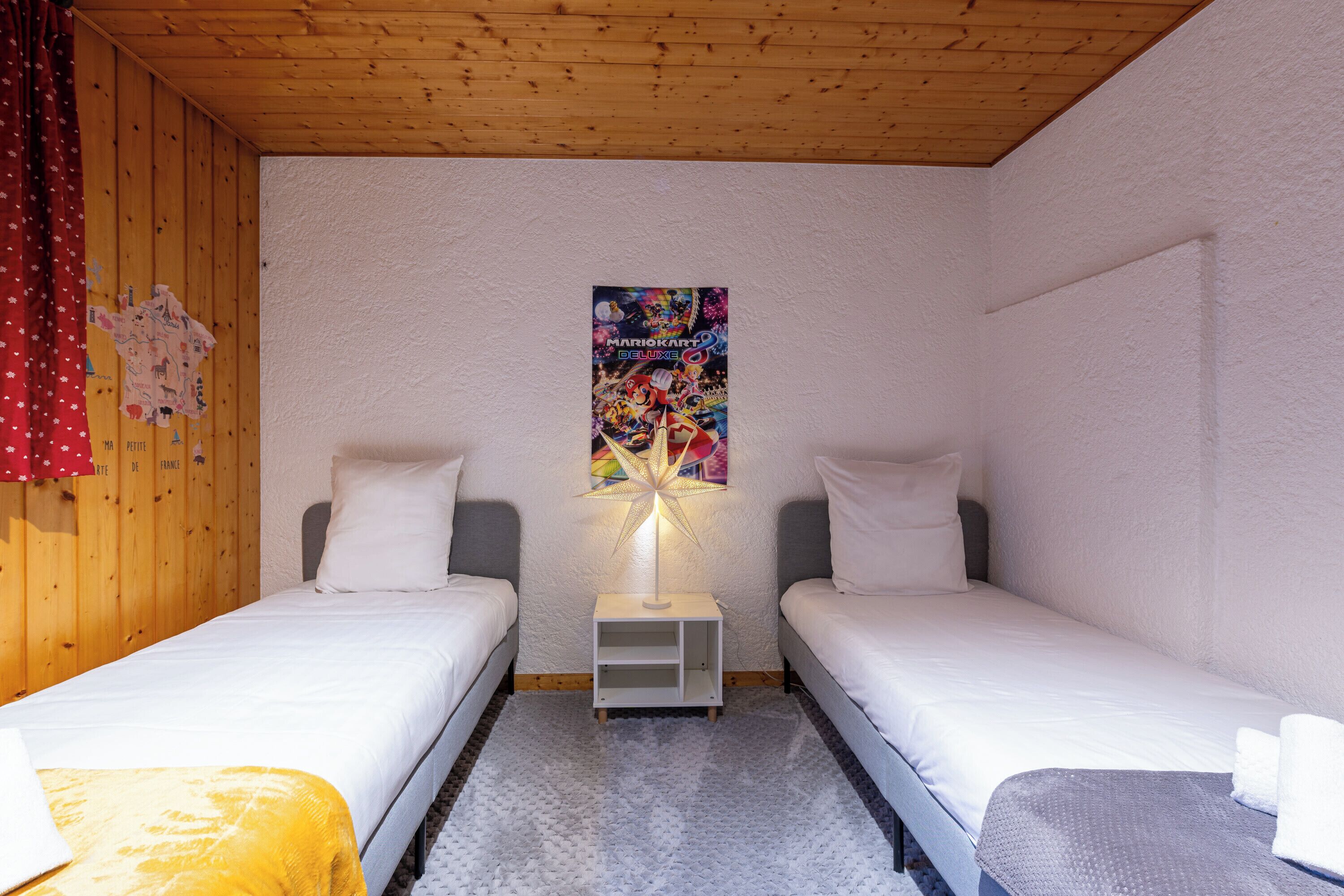 Quarto com duas camas de solteiro, mesa de cabeceira com abajur e um cartaz na parede.