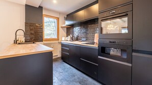 A modern kitchen with dark cabinetry, a large island, a built-in oven, and a window providing natural light.