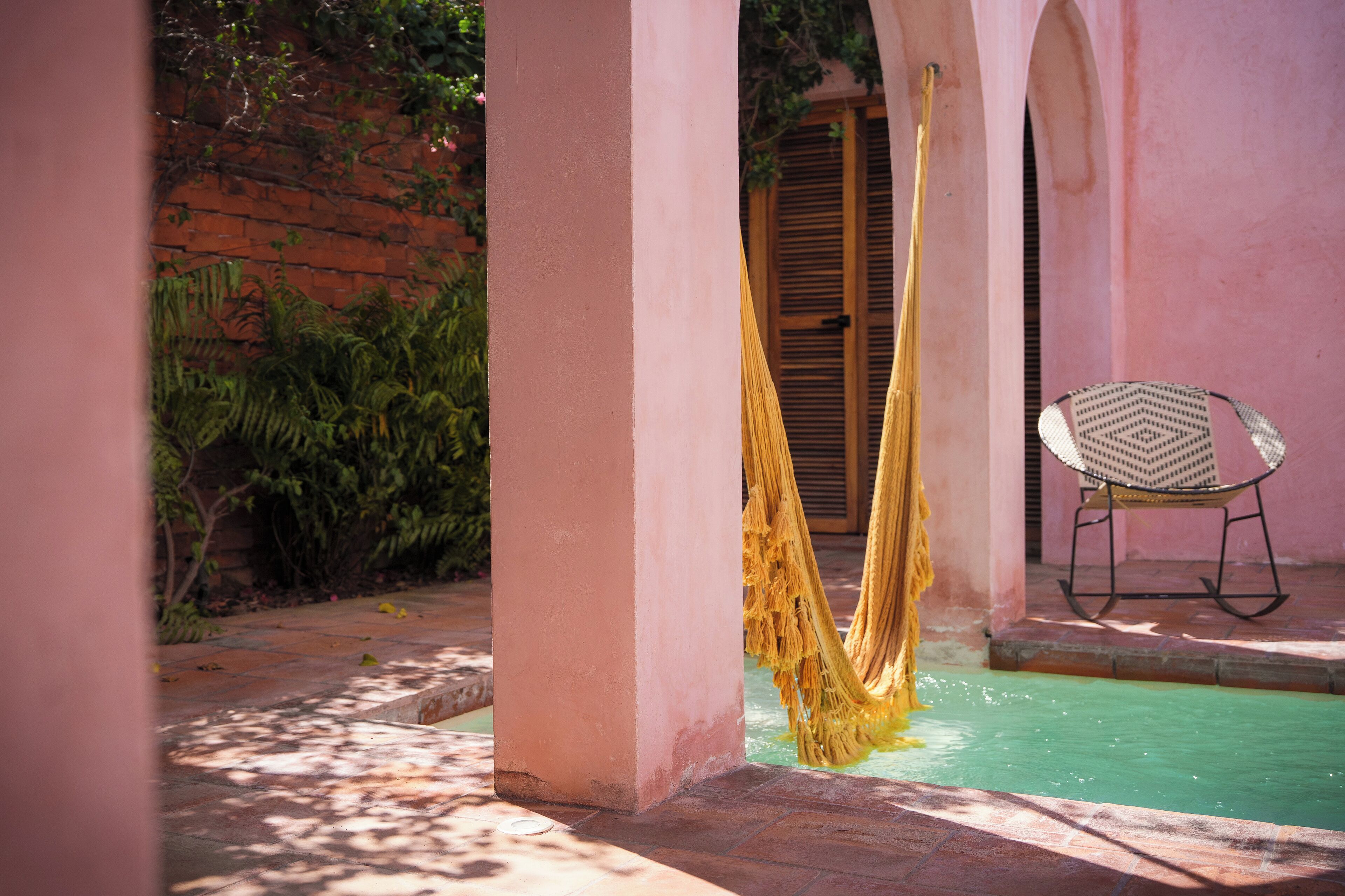 A pool area with a hammock, a chair, and a brick wall.