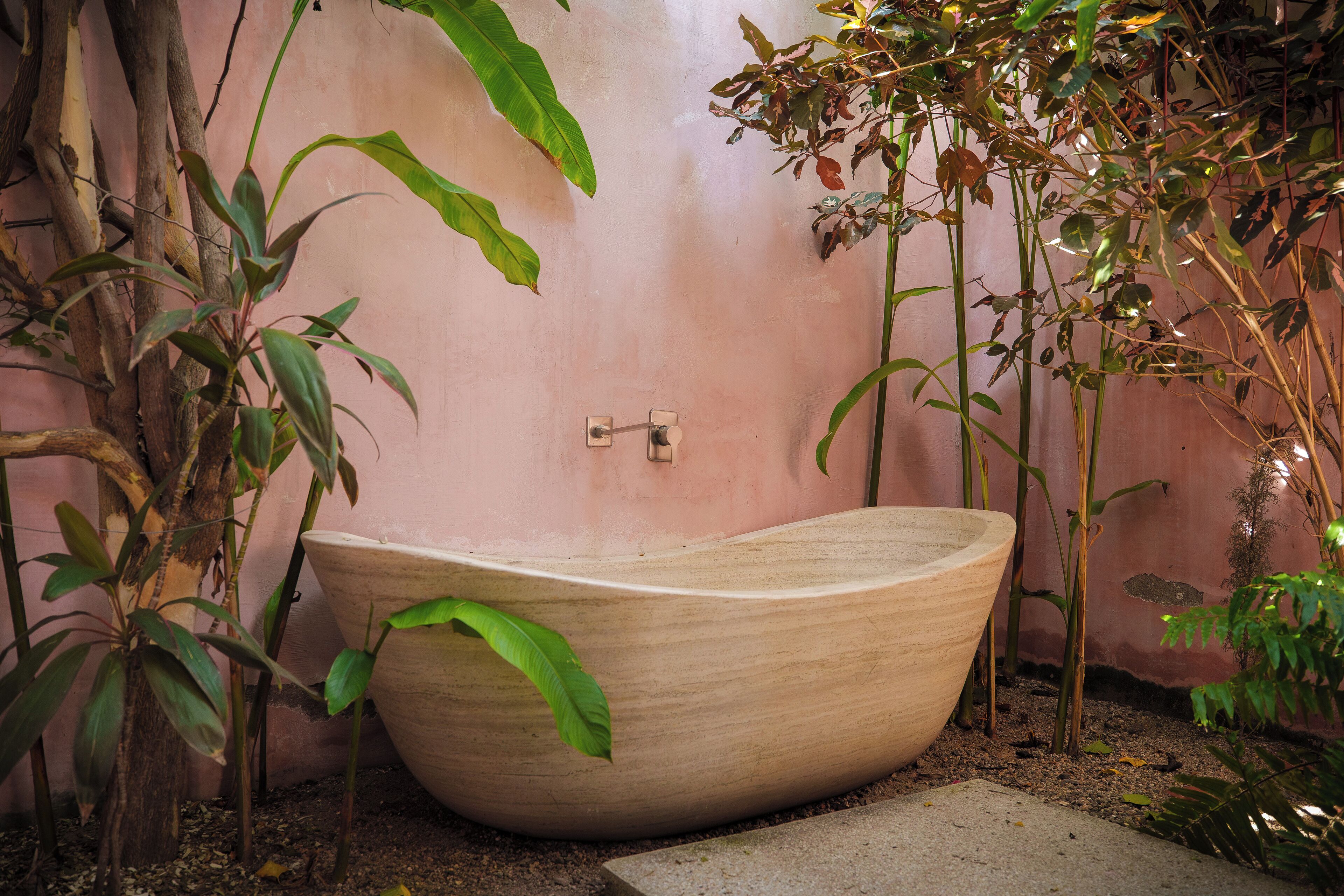 A large, wooden bathtub in a garden setting with various plants around.
