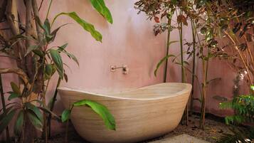 A large, wooden bathtub in a garden setting with various plants around.