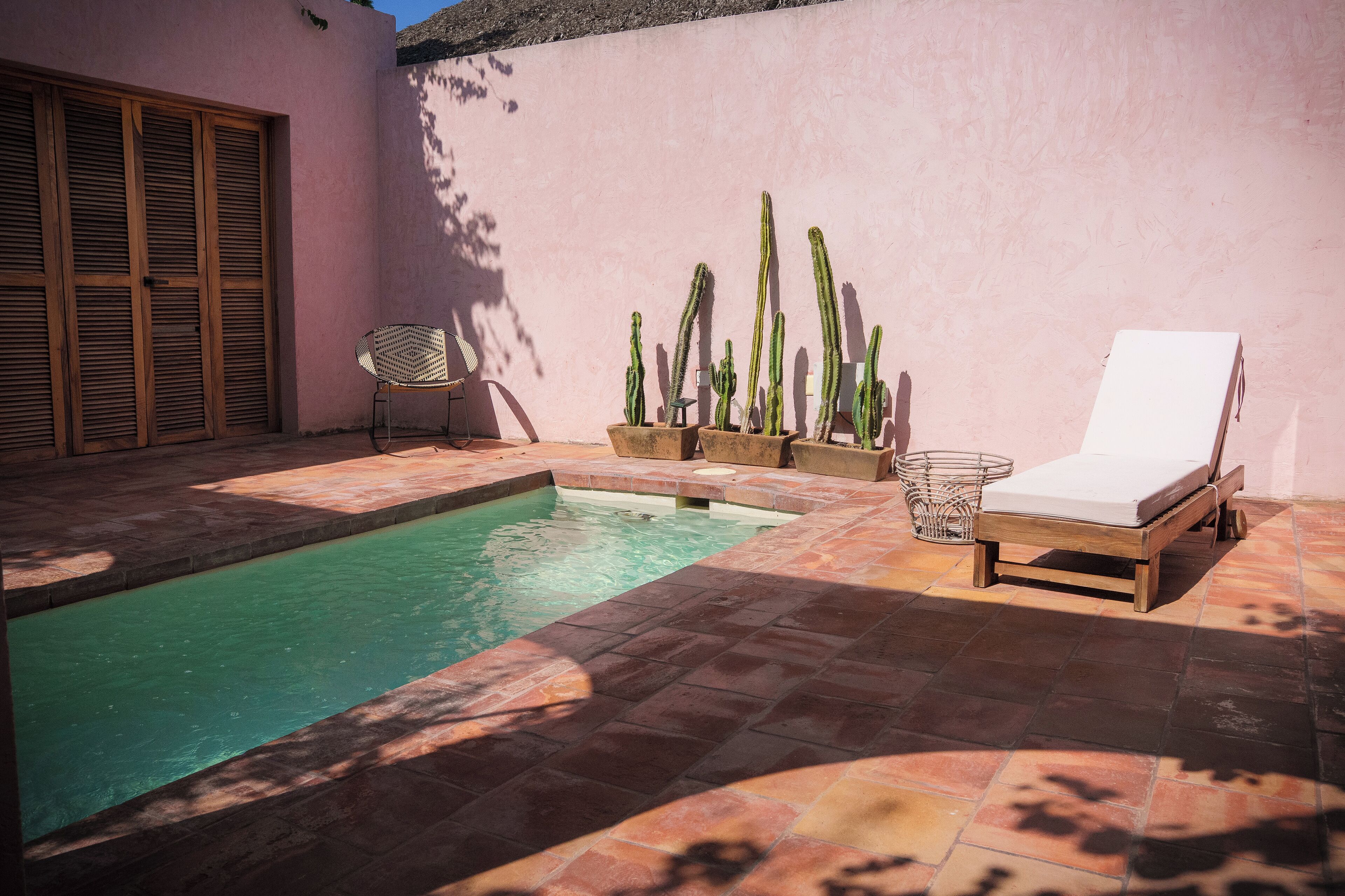 Zona de piscina amb una cadira de sol, cactus, una porta de fusta i un paviment de rajoles.