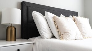 A neatly made bed with white bedding and decorative pillows, a bedside lamp, and a white nightstand. - Charming Retreat with Private Patio - Cozy and Convenient Escape (Indianapolis)