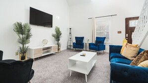 A modern living room with a flat-screen TV, blue and black chairs, a white coffee table, and a white console unit. - Charming Retreat with Private Patio - Cozy and Convenient Escape (Indianapolis)