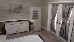 Et soveværelse med seng, kommode, et maleri, en dør med gardiner og en stenvæg.