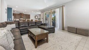 Un soggiorno moderno con un divano ad angolo, un tavolino in vetro e vista sulla cucina e sul patio.
