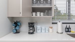 Cucina con mobili bianchi, una macchina da caffè e contenitori portaoggetti etichettati 'Caffè', 'Zucchero' e 'Tè'.