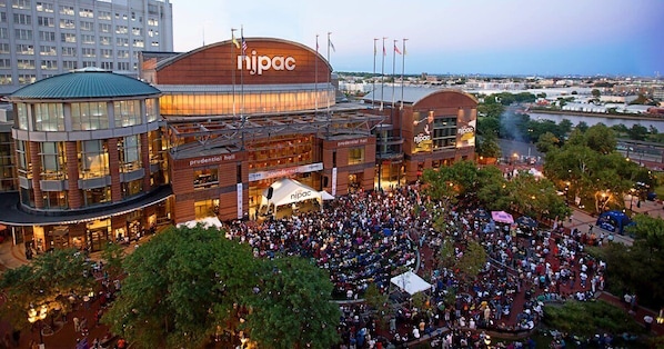 Un gran centro de convenciones con un cartel destacado que dice 'nipac', varios niveles y una multitud reunida en el exterior.