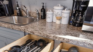 Un cajón de cocina con utensilios y recipientes etiquetados para té, café y azúcar.