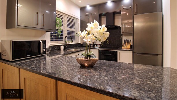 Una cocina moderna con electrodomésticos de acero inoxidable, encimera de granito y una orquídea en maceta.