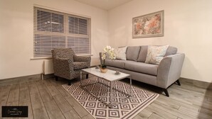 Un salón con un sofá gris, un sillón estampado y una mesa de centro con un jarrón de flores.