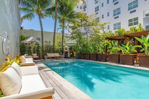 A pool area with lounge chairs, a wooden deck, and tropical plants. - Steps from Miami Attractions | Walkable South Beach Studio (Miami)