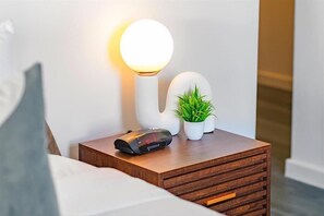 A bedside table with a clock, a lamp, and a potted plant. - Steps from Miami Attractions | Walkable South Beach Studio (Miami)