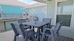 A covered outdoor patio with a table and chairs, a view of a neighboring house, and a window on the right.