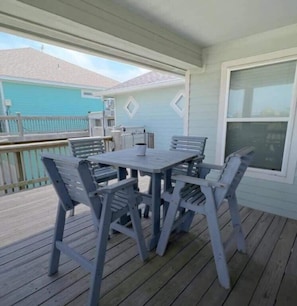 A covered outdoor patio with a table and chairs, a view of a neighboring house, and a window on the right.