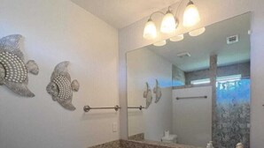 A bathroom with a granite countertop, two sinks, a large mirror, and decorative fish wall art.