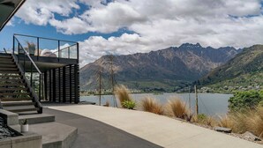 Ein moderner Außenbereich mit einer Treppe, die zu einem Glasgeländer, einer Betonplattform und einer Aussicht auf Berge und einen See führt.