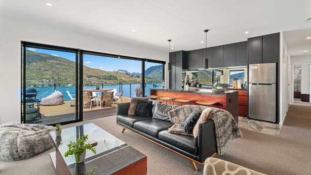 Eine moderne Küche mit einer großen Kochinsel, ein Essbereich mit Seeblick und ein Wohnzimmer mit Ledersofa und Glastisch.