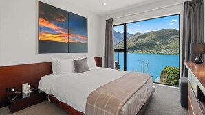 Ein Hotelzimmer mit einem großen Bett, einem Sonnenuntergangsbild, Blick auf einen See und einem hölzernen Kopfteil.