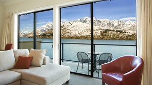 A modern room with a large sliding glass door leading to a balcony with a scenic mountain and lake view.