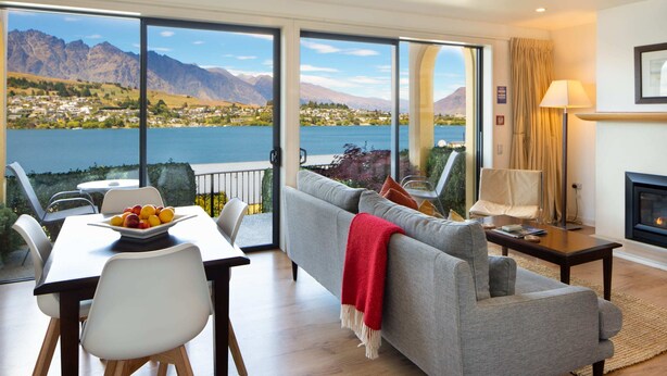 A living room with a sofa, a dining table with chairs, a fireplace, and a view of a lake and mountains.
