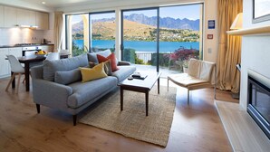 A modern living room with a grey sofa, a coffee table, and a view of a lake and mountains through large sliding doors.