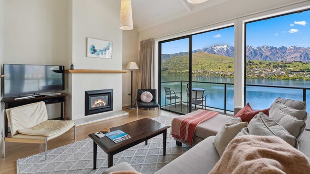 Una sala de estar moderna con chimenea, televisor y un amplio ventanal con vistas a un lago y montañas pintorescos.