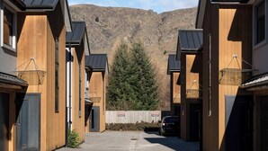 A row of modern wooden buildings with a mountain backdrop, a car parked in the driveway, and a sign indicating a private parking area. - Gallerie Coronet Summ (Queenstown)