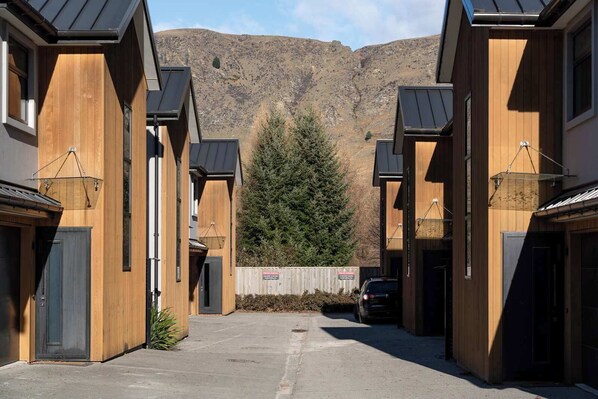 A row of modern wooden buildings with a mountain backdrop, a car parked in the driveway, and a sign indicating a private parking area.