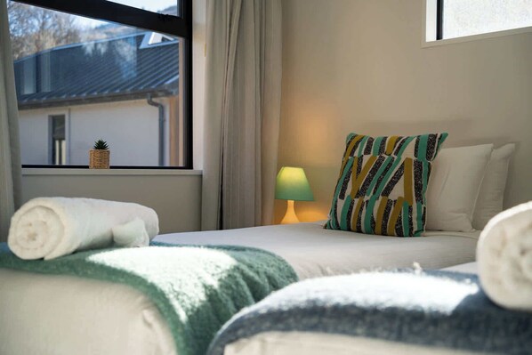 A hotel room with a bed, a window with curtains, a lamp, and a view of a building outside.
