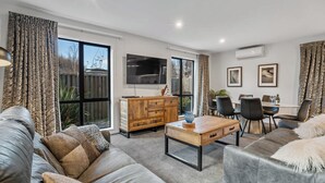 A modern living room with a sofa, coffee table, TV, and dining area. - Gallerie Coronet Summ (Queenstown)
