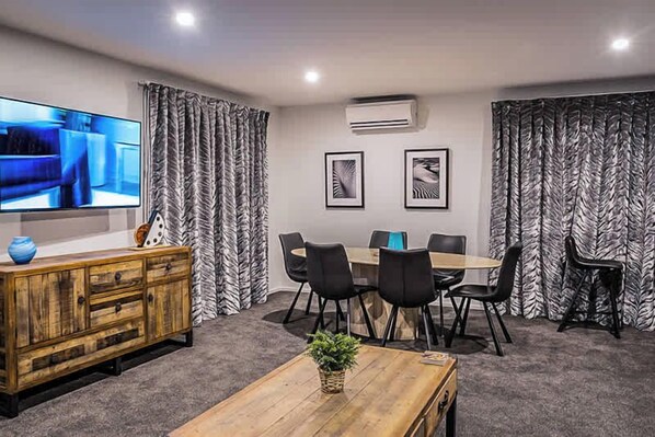 A conference room with a wooden table, black chairs, a TV on the wall, and zebra-patterned curtains.