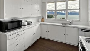 A modern kitchen with white cabinets, a microwave, toaster, and a view of a lake with mountains.