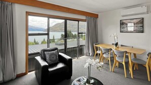 A modern hotel room with a large window offering a scenic view of mountains and a lake.