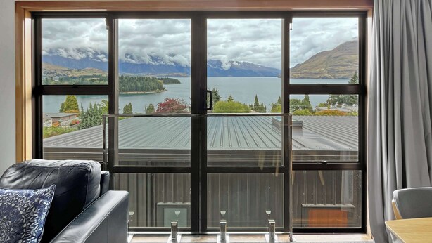 A room with a large window offering a view of a lake, mountains, and a distant island.