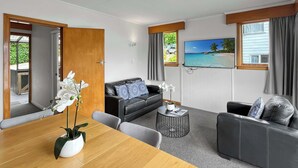 A modern living room with a wooden dining table, two sofas, a coffee table, and a TV mounted on the wall.