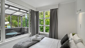 A modern bedroom with a large bed, grey bedding, and a view of a balcony with outdoor furniture.