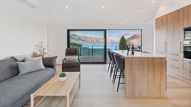 Un salon moderne avec un canapé, une table basse et une vue sur les montagnes, visible à travers de grandes fenêtres.